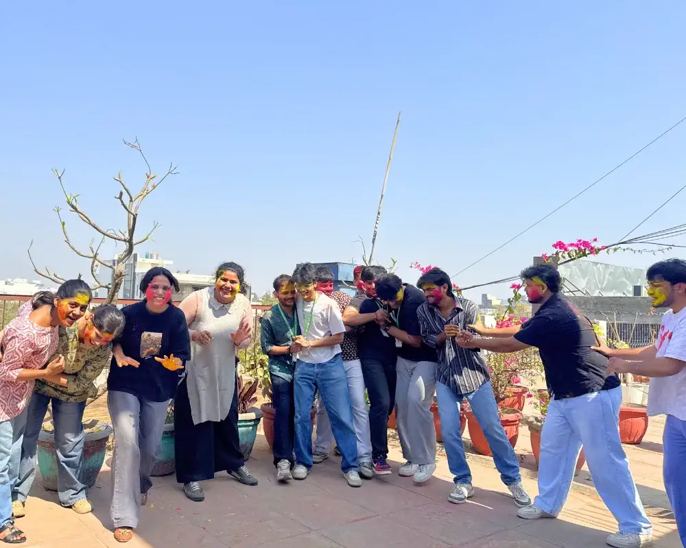 Career Plan B team celebrating Holi with vibrant colors on a sunny rooftop under a clear blue sky.