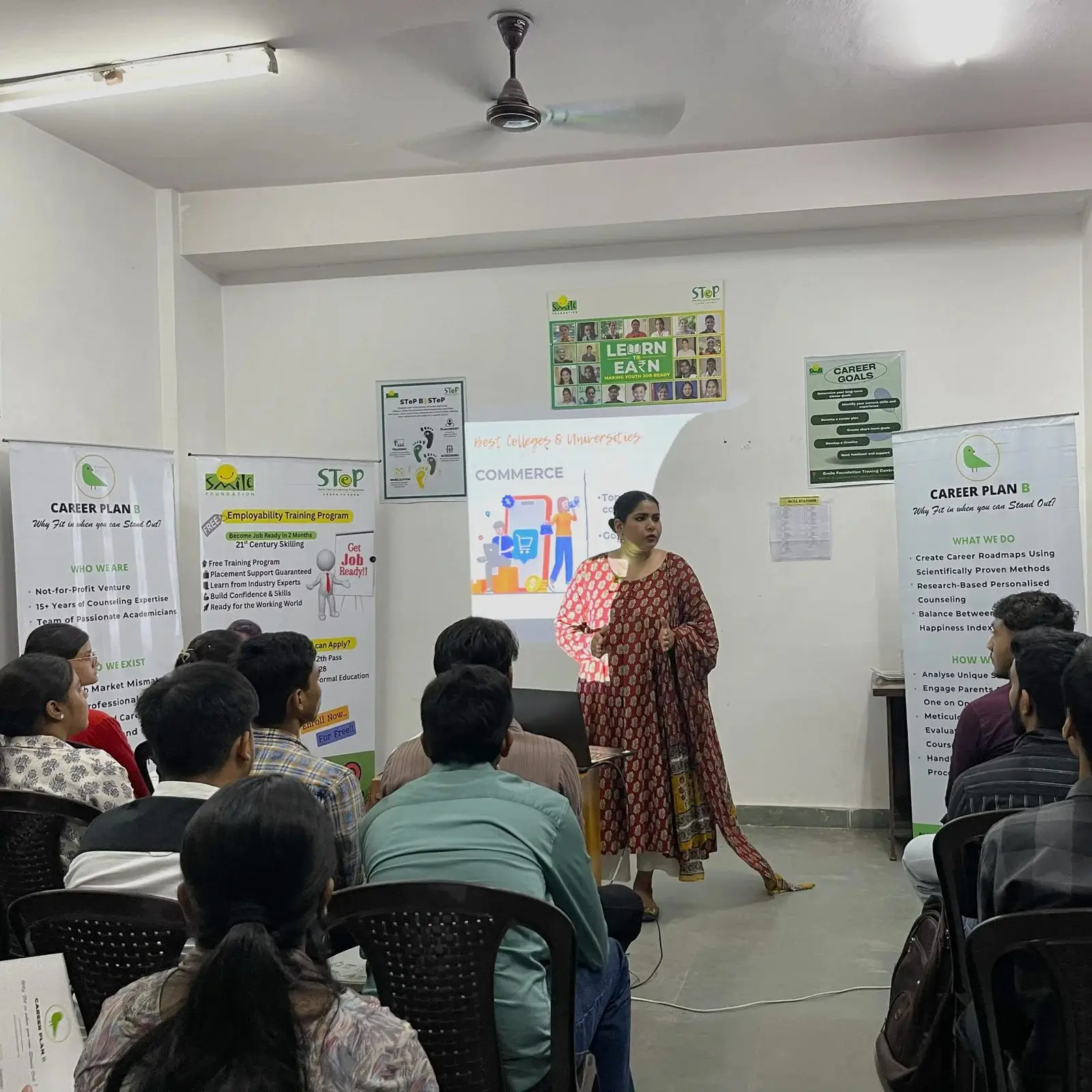 Career Plan B founder presenting a commerce career seminar to students in a classroom with Smile Foundation banners.