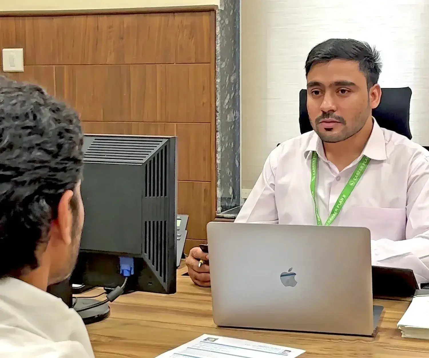 Academic counsellor with Career Plan B lanyard speaking to a student across a desk with a laptop.
