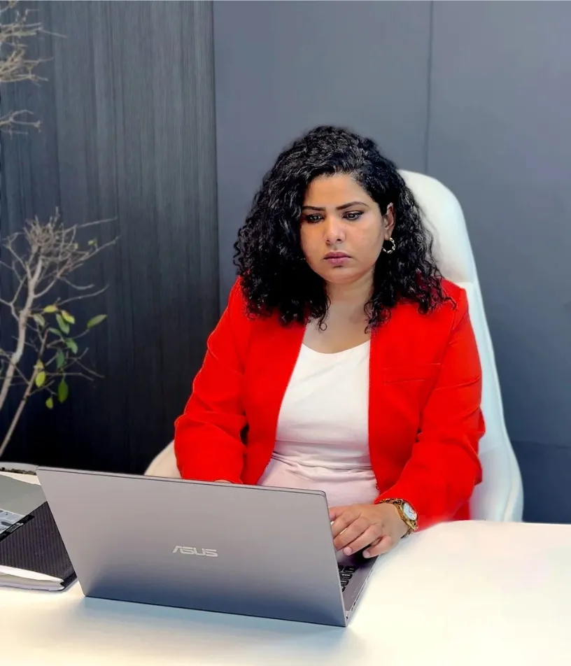 Career counsellor in a red blazer working on a laptop at a desk in a professional office setting.