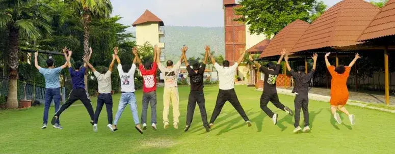 Career Plan B team jumping in the air with arms raised on a green lawn at a sunny resort during a company retreat.
