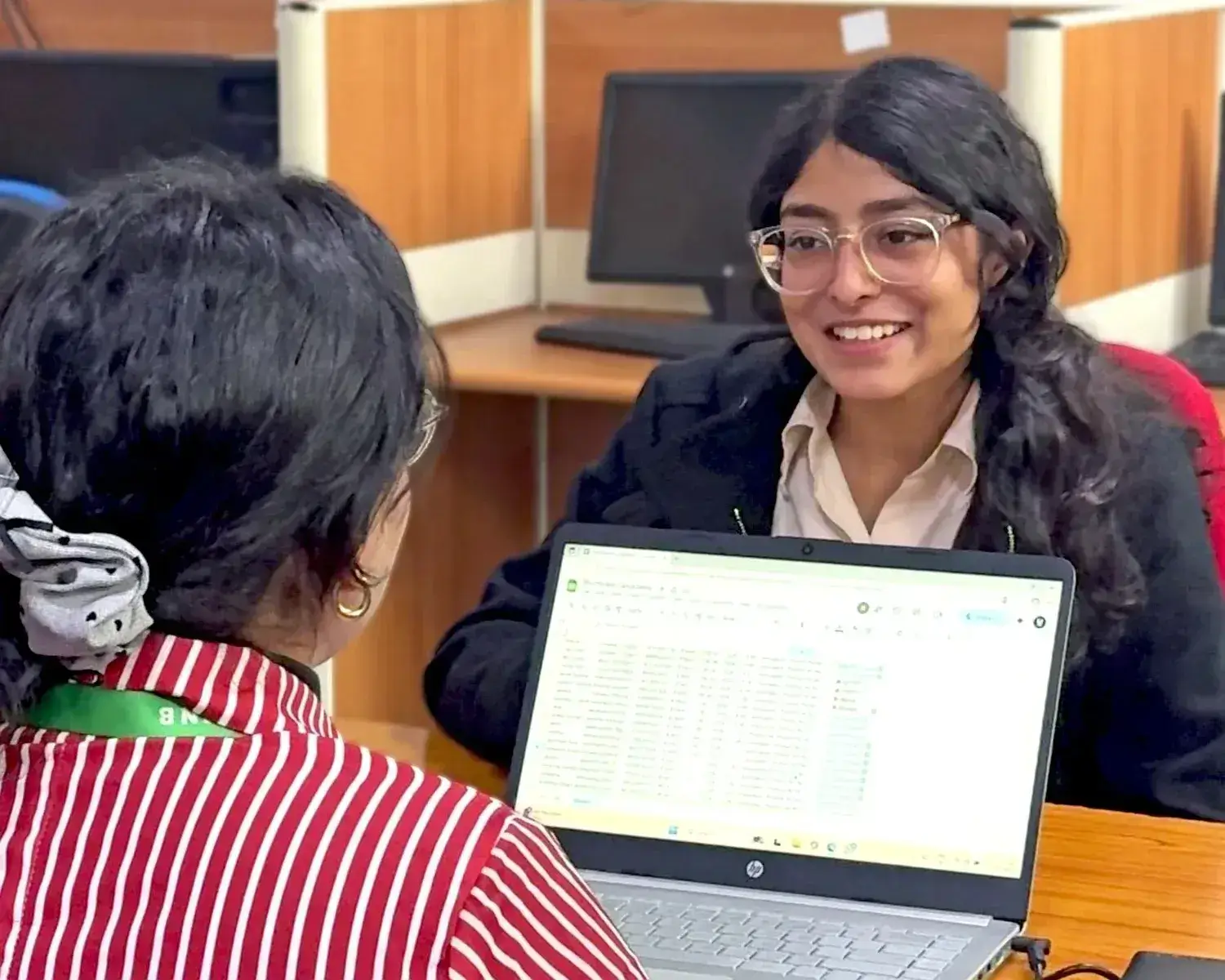 Smiling student taking counselling from a career expert using a laptop to review data in a modern office cubicle.
